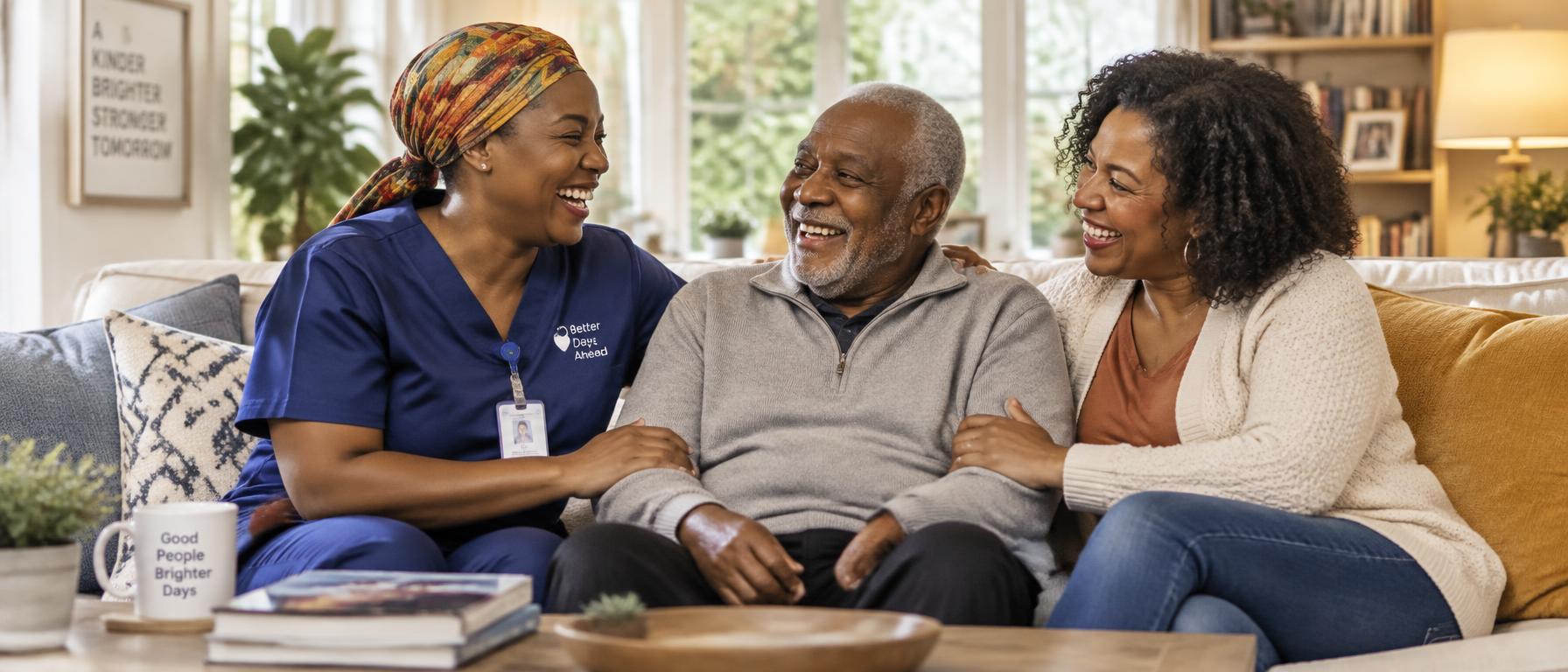 A caregiver laughing with an older man and his daughter together on a sofa in a bright home living room